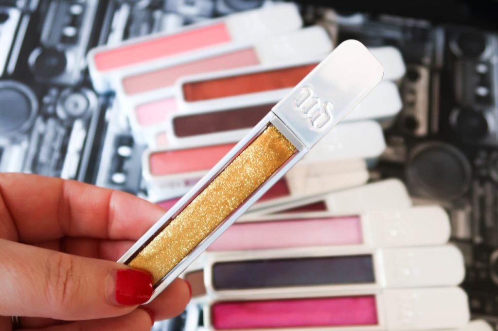 A bright gold lip gloss in-front of other lip glosses